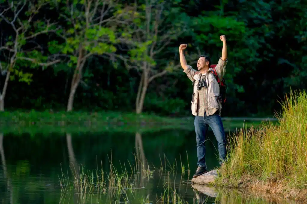 overcome an addiction - man standing by a lake feeling accomplished