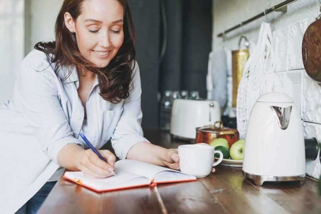 Woman writing in a notebook at her kitchen counter while planning a gradual Suboxone taper